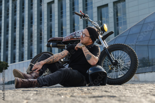 Shot of individual motorcycle driver posing near huge city building.