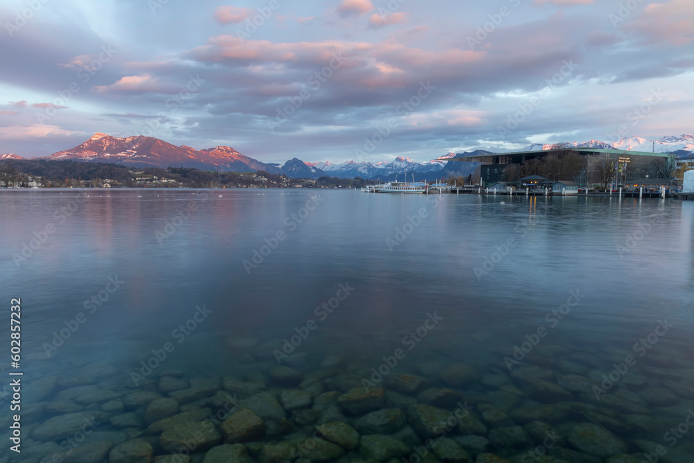 Beautiful landscape of Luzern lake in Switzerland with swiss alps snow cap mountain background in winter.Smooth water and space stone or rock foreground.Tourist travels in Europe.Twilight sky. 