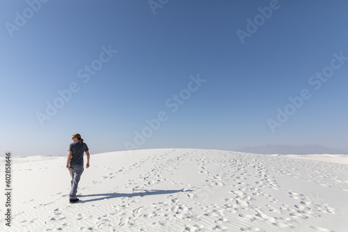 Woman walking away from camera over white sand dune