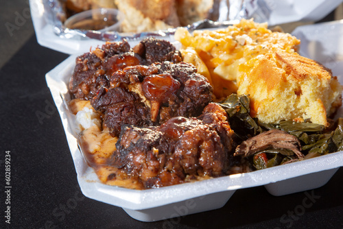 A view of an entree of smothered oxtails, with a side of mac n cheese, corn bread, and collard greens.