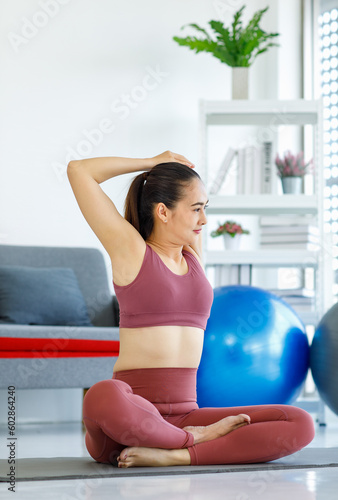 Asian pretty healthy fit slim sexy female sporty athlete model in sports bra and leggings sitting crossed legs stretching arms and hands on yoga mat warm up ready to workout exercise in living room