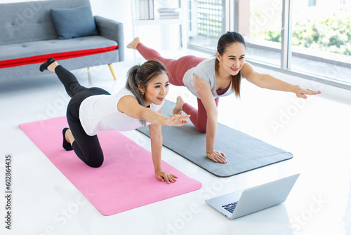 Two Asian healthy fit slim sexy female sporty athlete model friend in sportwear and leggings laying down planking on yoga mat together watching online streaming workout lesson via laptop computer