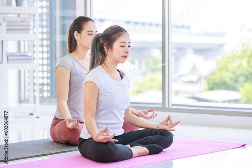 Two people Asian beautiful healthy fit slim female sporty athlete model in sport bra and leggings sitting crossed legs in lotus posture on yoga carpet smiling doing meditation in living room at home Free Download Two people Asian beautiful healthy fit slim female sporty athlete model in sport bra and leggings sitting crossed legs in lotus posture on yoga carpet smiling doing meditation in living room at home - GFXLoad