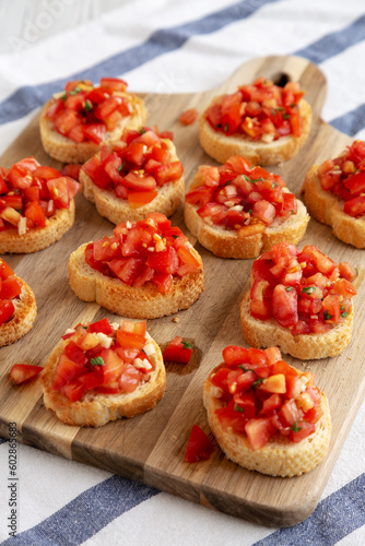 Homemade Italian Bruschetta Appetizer with Fresh Basil and Juicy Tomatoes on a Wooden Board, side view.