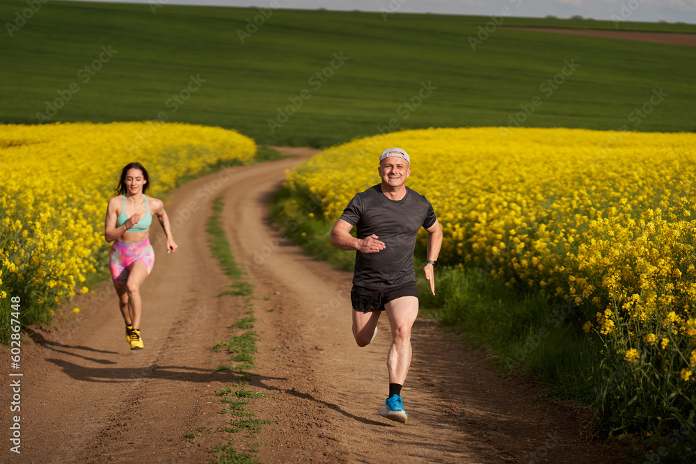 Obraz premium Endurance runners on a dirt track in a canola field, training