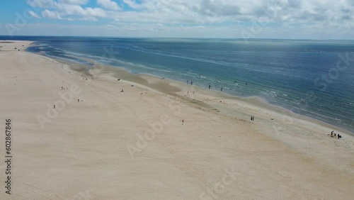 People play and relax on wide spread of golden sand and calm ocean in Denmark, sonderstrand beach aerial photo