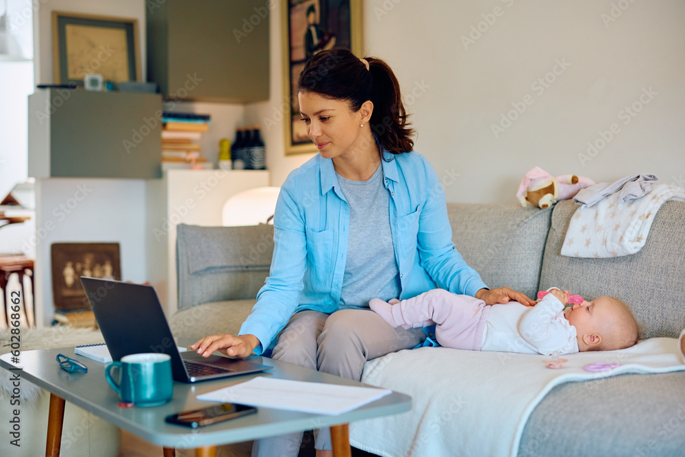 Obraz premium Working mother using laptop while being with her baby at home.