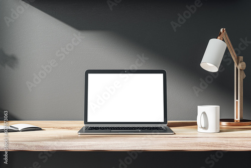 Front view on blank white modern laptop monitor with space for web design, website or landing page on wooden work table with coffee mug and sunlit black wall background. 3D rendering, mock up