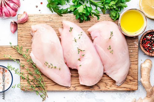 Photographie Raw chicken fillet on rustic wooden cutting board prepared for cooking with garlic, thyme, spices and pepper