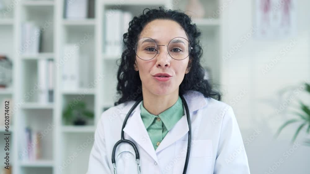 Webcam view. Close up of a smiling female doctor talking on a video call looking at the camera in hospital clinic. A happy medical worker physician consults a patient while sitting in a modern office Webcam view. Close up of a smiling female doctor talking on a video call looking at the camera in hospital clinic. A happy medical worker physician consults a patient while sitting in a modern office
