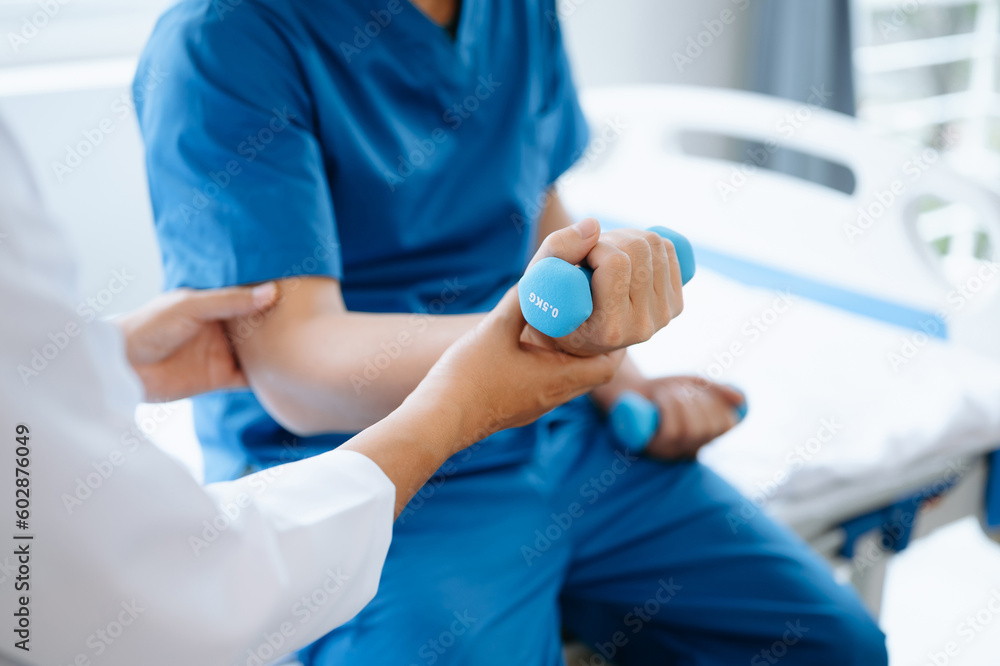 Asian physiotherapist helping male patient stretching arm during exercise correct with dumbbell in hand during training hand in hospital office. Asian physiotherapist helping male patient stretching arm during exercise correct with dumbbell in hand during training hand in hospital office.