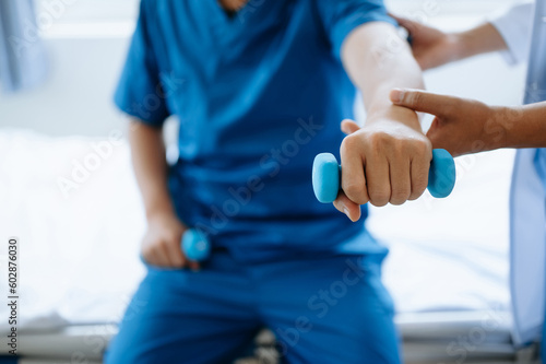 Asian physiotherapist helping male patient stretching arm during exercise correct with dumbbell in hand during training hand in hospital office.