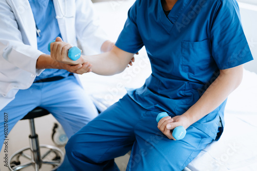 Asian physiotherapist helping male patient stretching arm during exercise correct with dumbbell in hand during training hand in hospital office.