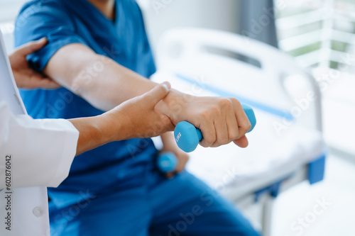 Asian physiotherapist helping male patient stretching arm during exercise correct with dumbbell in hand during training hand in hospital office.