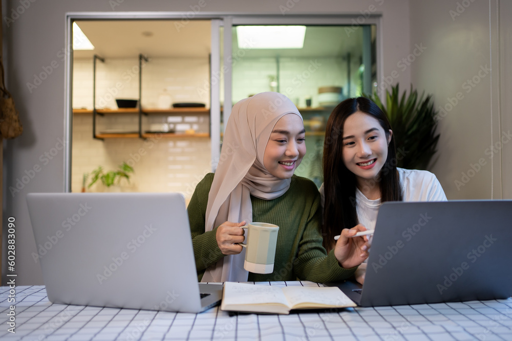 Cheerful girlfriends in had near face smiling while planning further work together and using laptop at home. Cheerful girlfriends in had near face smiling while planning further work together and using laptop at home.