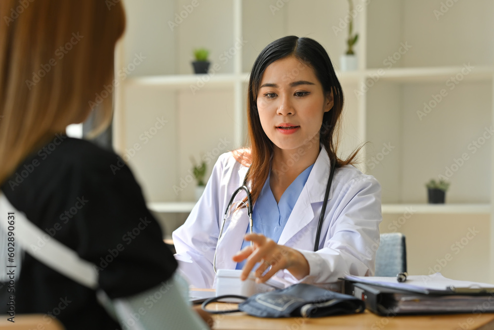 Female bone specialist in white cuneiform consulting with injured female with sling on shoulder. Rehabilitation and healthcare concept Female bone specialist in white cuneiform consulting with injured female with sling on shoulder. Rehabilitation and healthcare concept