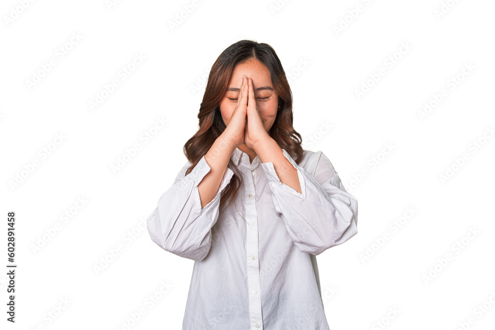 A young chinese woman holding hands in pray near mouth, feels confident. A young chinese woman holding hands in pray near mouth, feels confident.