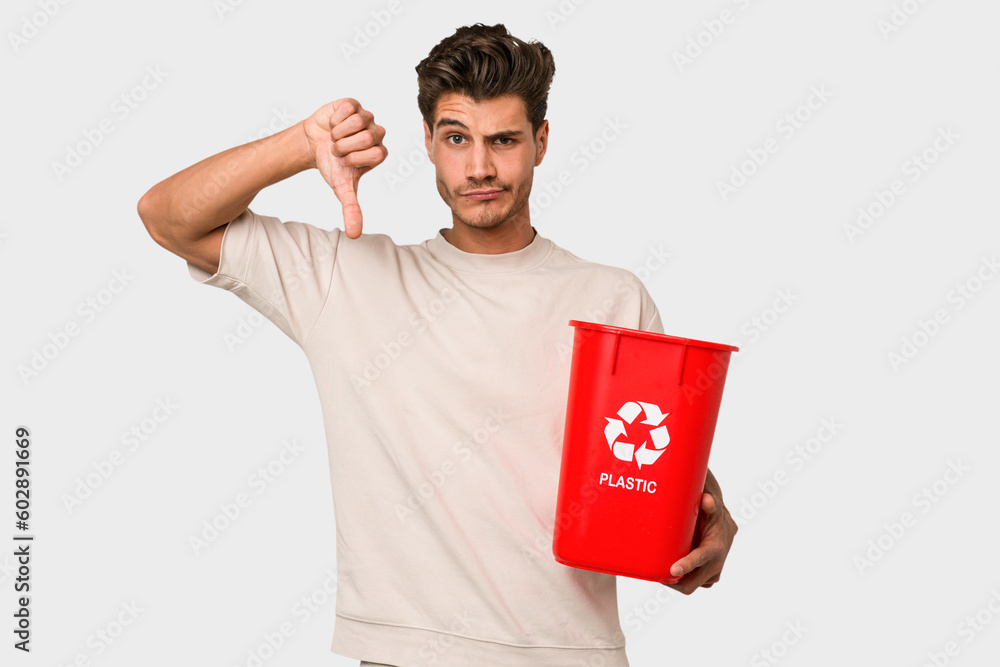 Young caucasian man holding a plastic trash isolated showing a dislike gesture, thumbs down. Disagreement concept. Young caucasian man holding a plastic trash isolated showing a dislike gesture, thumbs down. Disagreement concept.