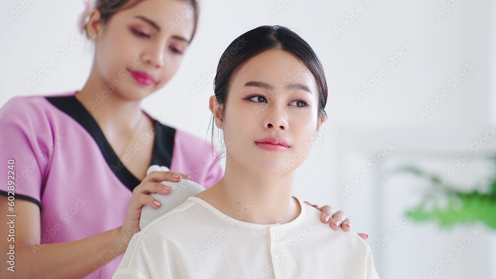 Asian women sitting on massage bed and relax during back massage with herbal balls by woman masseuse. Traditional thai herbal massage Asian women sitting on massage bed and relax during back massage with herbal balls by woman masseuse. Traditional thai herbal massage
