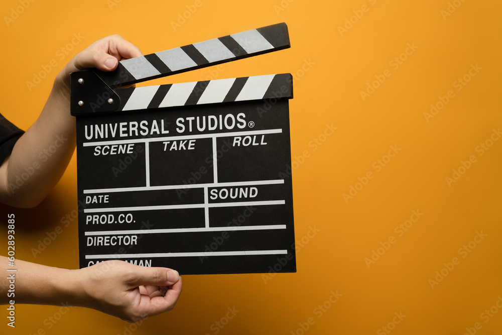 Hands holding black clapperboard on yellow background. Video production, film, cinema industry concept