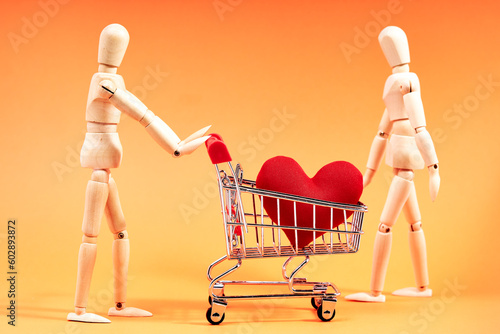 Dummy pushing a shopping cart with a red heart on orange background