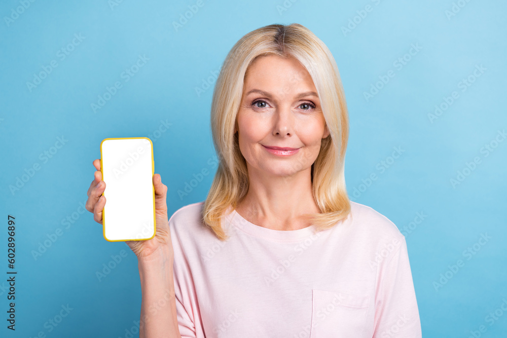 Photo of cheerful lovely lady hand hold demonstrate empty space smart phone display isolated on blue color background Photo of cheerful lovely lady hand hold demonstrate empty space smart phone display isolated on blue color background