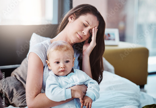 Stress, headache and a a mother with her baby in a bedroom of their home together in the morning. Children, family and burnout with a tired mama sitting on a bed with an infant son as a single parent
