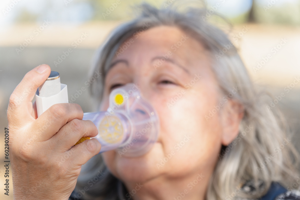woman uses a nebulizer inhaler for the treatment of respiratory diseases. she is in the countryside breathing fresh air and enjoying the sun.