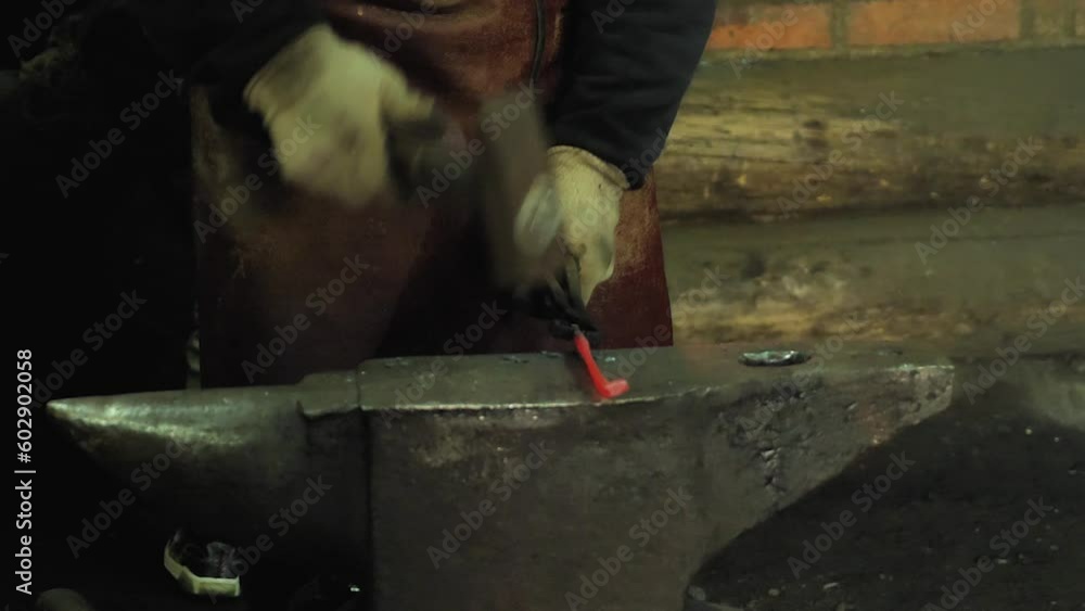 The blacksmith's hands striking the hot metal with a hammer. A professional blacksmith forging molten metal on an anvil in the forge. Close up. In slow motion The blacksmith's hands striking the hot metal with a hammer. A professional blacksmith forging molten metal on an anvil in the forge. Close up. In slow motion