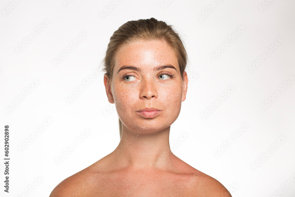 Obraz premium Pretty girl with freckles looks away with her hair tied up in front of the camera on a white background