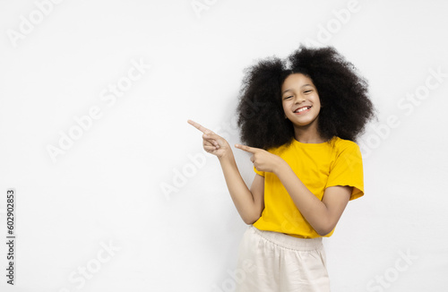 Portrait happy girl with afro hairstyle wear yellow T-shirt points a side into empty space. Advertisement concept. Area to enter message with white background. Copy space For text advertisement. © eakgrungenerd