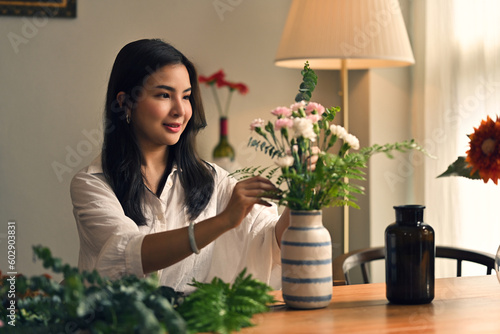 Obraz na plátně Gorgeous Asian woman enjoys her free time at home, arranging a vase with flowers