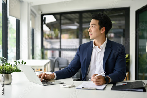 Handsome businessman sits at his office desk, looking out the window and daydreaming