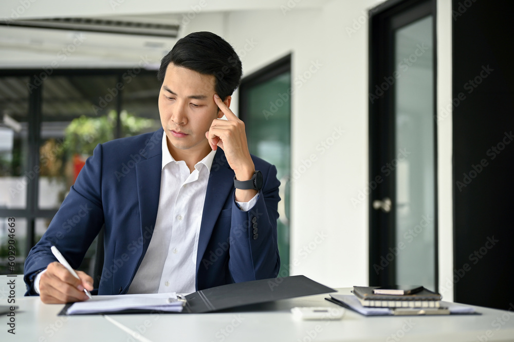Stressed Asian businessman examining financial reports, working at his desk. Stressed Asian businessman examining financial reports, working at his desk.