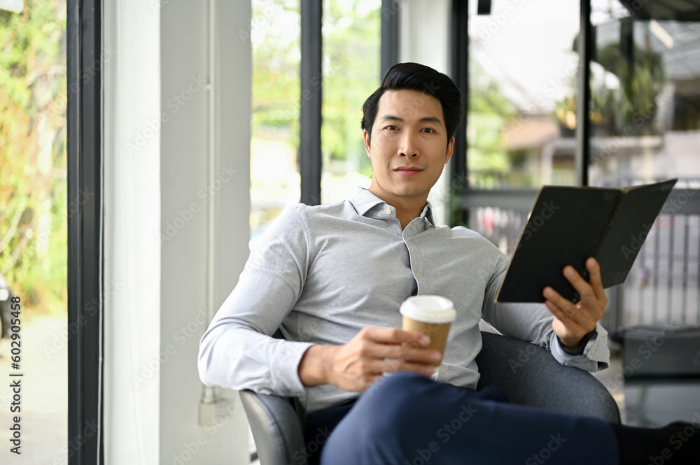 Handsome Asian businessman sits in an office lounge with his notebook and coffee cup Handsome Asian businessman sits in an office lounge with his notebook and coffee cup