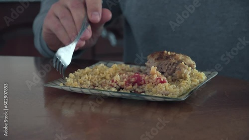 Close-up, Plate with Bulgur and Cutlet, with Red Sauce. Male Hands with a Fork. Food Culture and Diet. Man Eats Rice and Cutlet photo