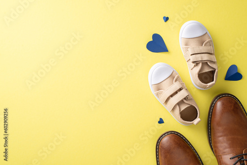 Father's Day wishes from son and dad. Top view of leather shoes, tiny baby sneakers, and hearts, on yellow background with space for logo or message