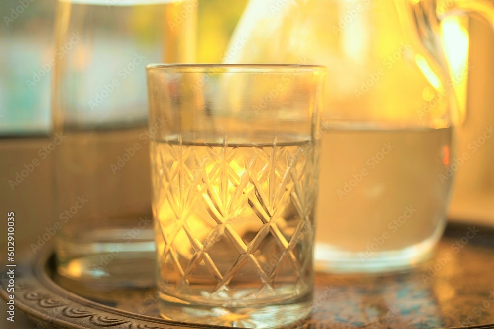 Glass of water and jug of water in a tray on the sunny windowsill. Glass of water and jug of water in a tray on the sunny windowsill.