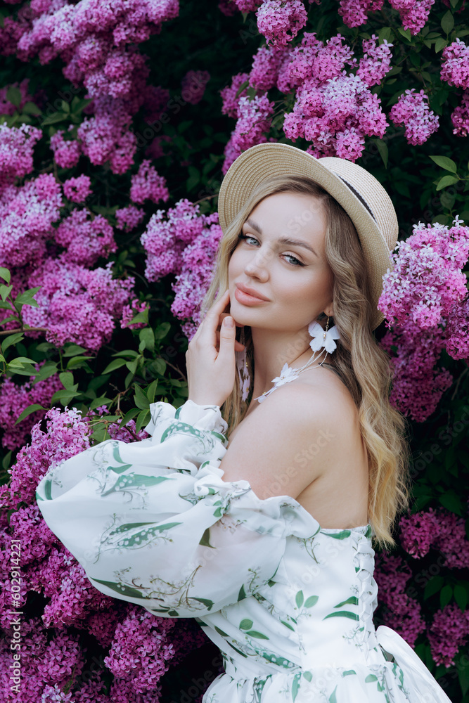 Fototapeta premium Beautiful, stylish, cute blonde in a white dress with a green pattern as a model for a photo shoot in lilac. They made luxurious portraits of her in the green garden of the park.