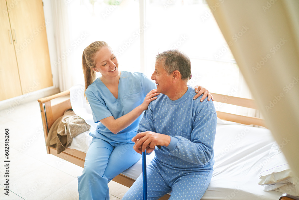 Female caregiver sitting with elderly man on bed at rehab center Female caregiver sitting with elderly man on bed at rehab center