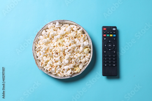 a bowl of popcorn and remote control. Entertainment concept on blue background.
