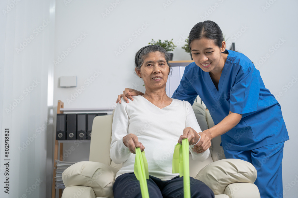 Fototapeta premium Concept of World Confederation for Physical Therapy. young physiotherapist caregiver helping mature elderly woman training with elastics in rehabilitation center, muscle weakness