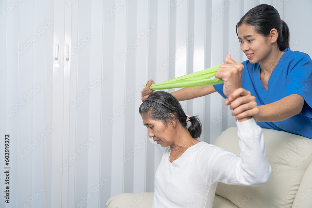 Concept of World Confederation for Physical Therapy. young physiotherapist caregiver helping mature elderly woman training with elastics in rehabilitation center, muscle weakness Concept of World Confederation for Physical Therapy. young physiotherapist caregiver helping mature elderly woman training with elastics in rehabilitation center, muscle weakness