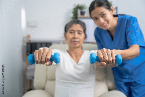 Young pretty asian physiotherapist helping senior female patient holding dumbbell in physical therapy session, concept of World Confederation for Physical Therapy.