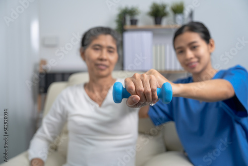 Young pretty asian physiotherapist helping senior female patient holding dumbbell in physical therapy session  concept of World Confederation for Physical Therapy.