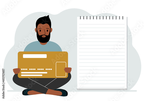 A man sits cross-legged in his hands holding a large credit card next to a close-up notepad for text. Concept of credit card, expense planning, income planning.