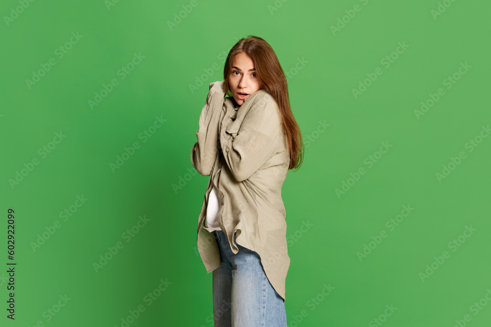 Portrait of emotive, frightened, young girl holding hands together with open mouth over green color studio background. Scared person Portrait of emotive, frightened, young girl holding hands together with open mouth over green color studio background. Scared person