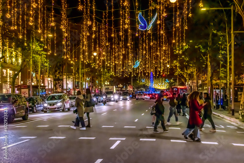 Barcelona, Spain - November 26,2021: Blue glowing butterflies and golden garlands hang over the road on Passeig de Gracia in Barcelona at night. Cars and people move under festive illumination at dusk