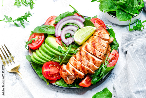 Healthy vegetable salad with grilled chicken fillet, spinach, tomatoes, avocado and onion with olive oil on white table background. Tasty detox, ketogenic diet food. Top view