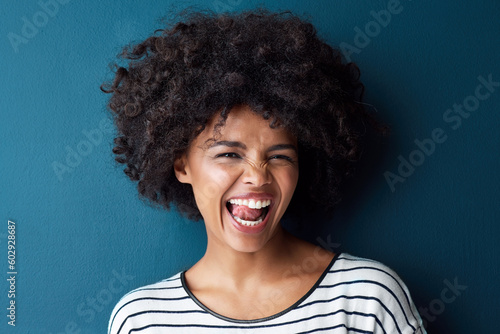 Fotografie Portrait, funny and woman with tongue out, silly and happiness against a blue studio background